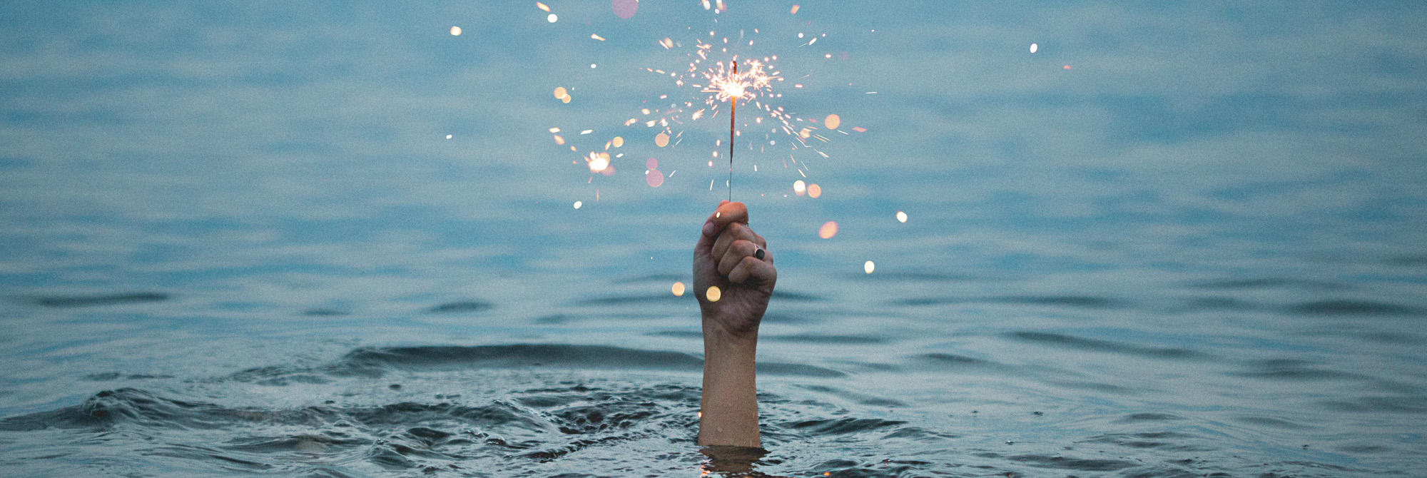 A woman under the water holding a sparkler.