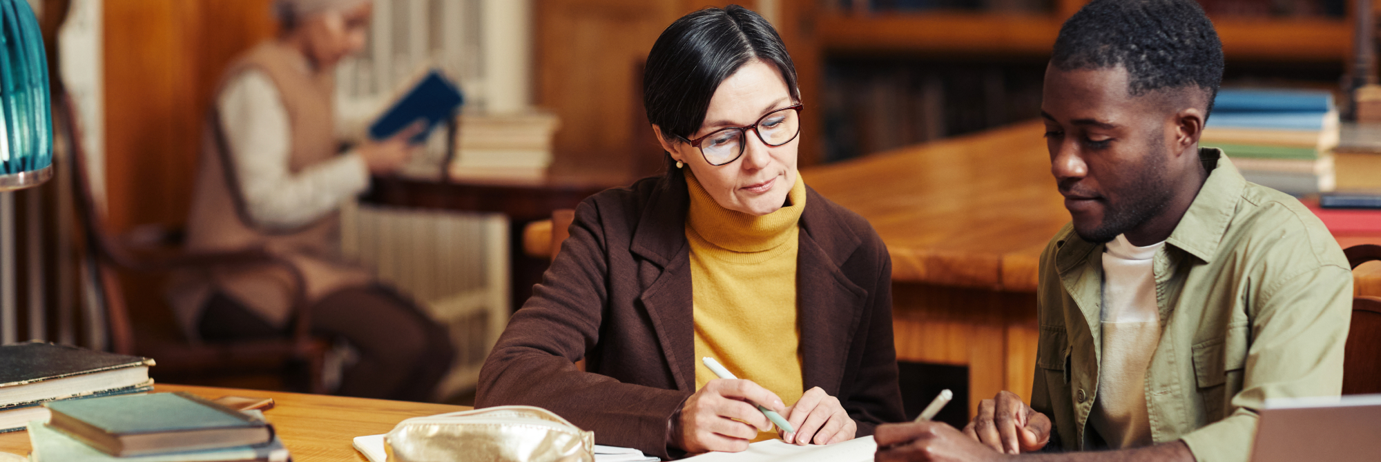 A student and supervisor discussing notes in a library, illustrating effective collaboration for an Extended Essay (EE).