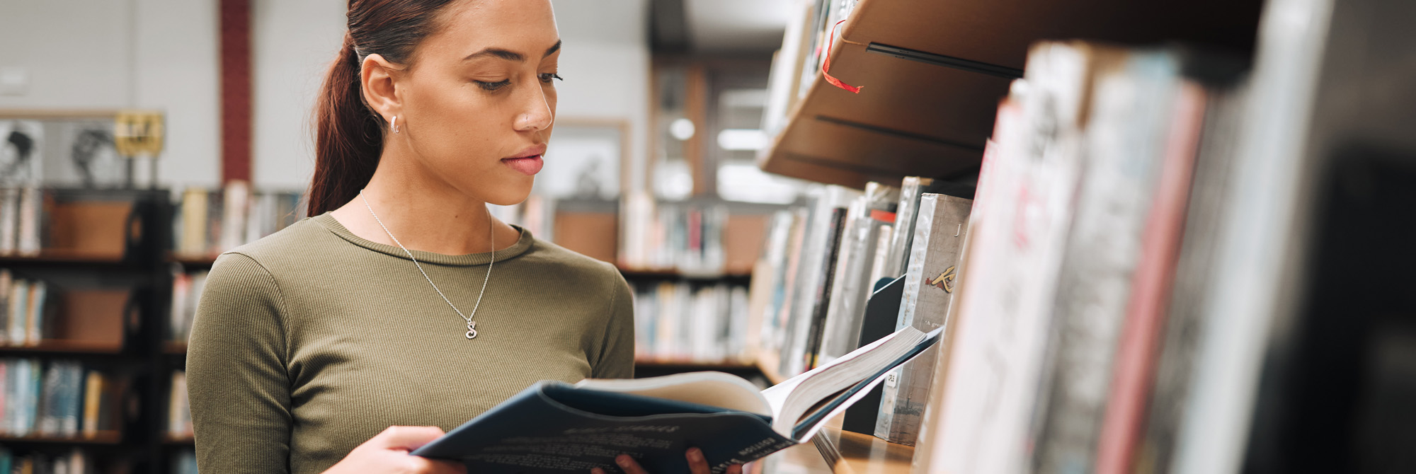 Black woman reading book about IB English Oral Commentary in a library.